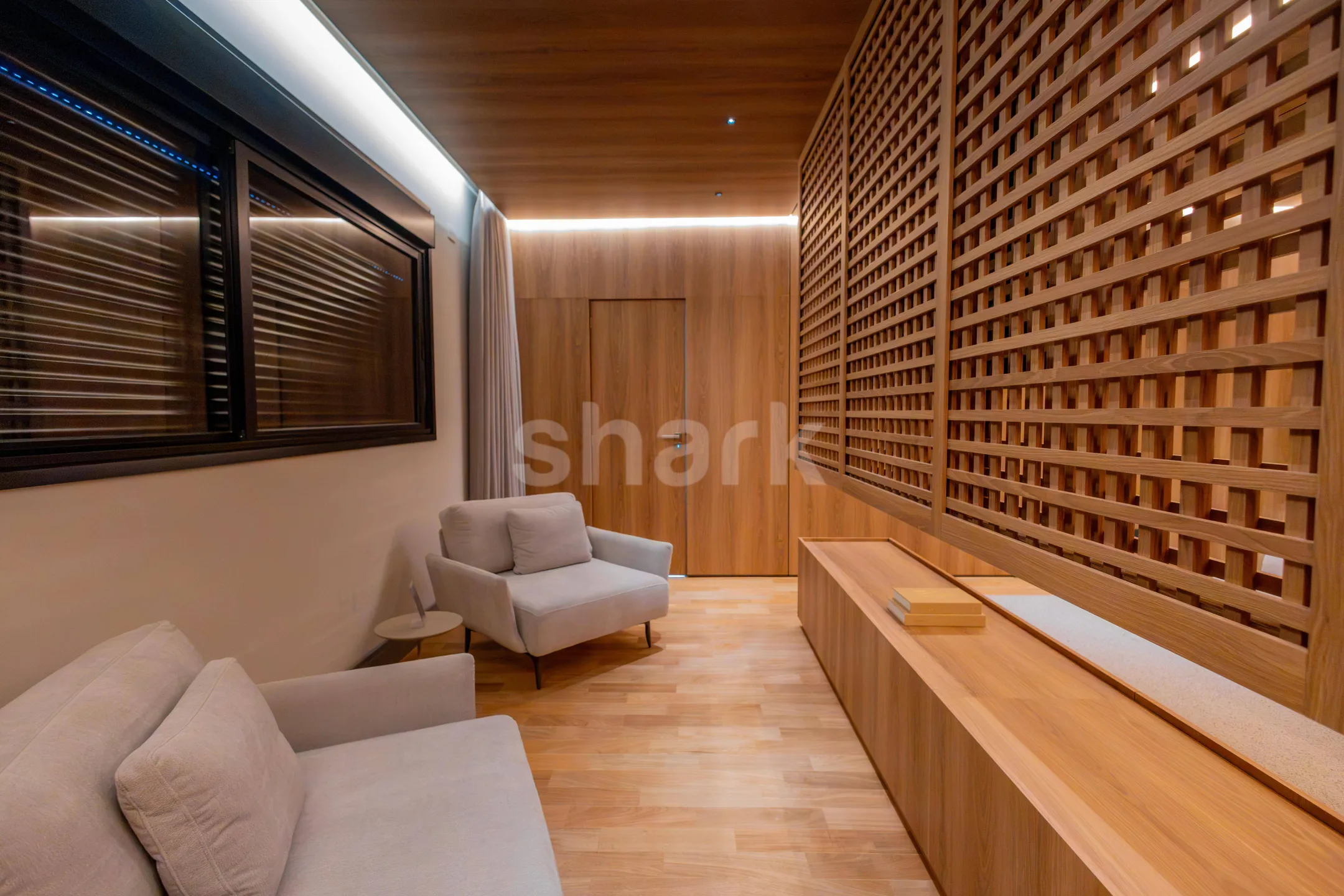 Estar da suíte master com poltronas e painel de madeira vazado